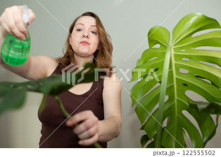 A woman cares for her houseplant using a spray bottle for hydration and proper care 122555502