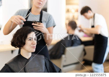 Female hairdresser giving haircut to adult woman Female hairdresser giving haircut to adult woman 122555875