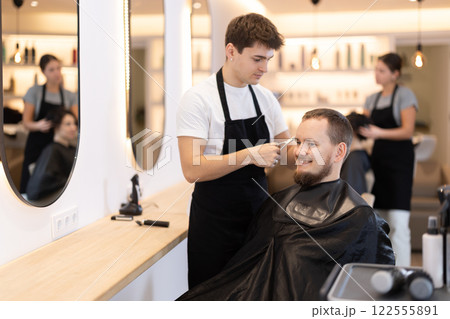 Young guy hairdresser giving haircut to young man 122555891