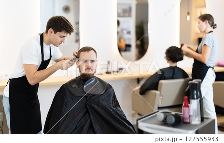 Young guy hairdresser giving haircut to young man 122555933