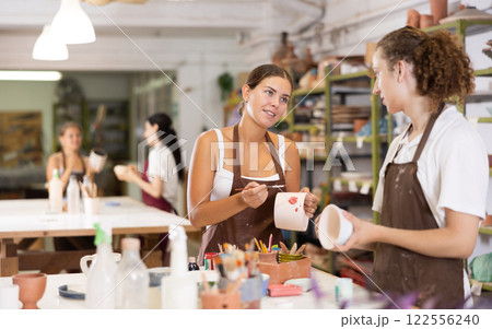 Young man sits near table and decorates clay ceramic craft vase, plate 122556240