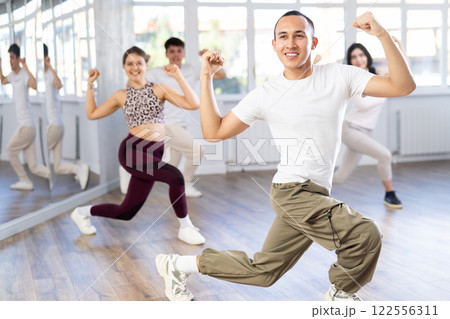 Positive woman and man engaged in dancing in group practices energetic swing in dance studio Positive woman and man engaged in dancing in group practices energetic swing in dance studio 122556311