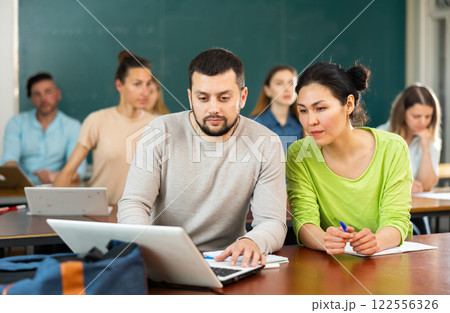 Man and woman helping each other to solve problem on laptop while studying in university class 122556326