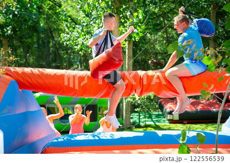 Cheerful teenager having fun with father on inflatable pillow fight arena 122556539