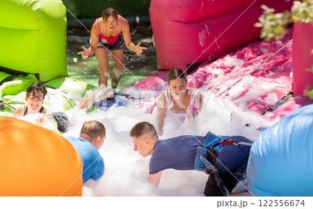 Cheerful friends picking up balls in inflatable pool full of foam Cheerful friends picking up balls in inflatable pool full of foam 122556674