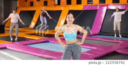 Portrait of cheerful young female in sportswear posing and smiling at camera on colorful trampoline in game club 122556742