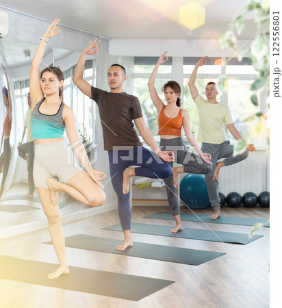 Girl in sportswear exercising with group multinational people at yoga studio, standing in warrior one leg pose on fitness mat 122556801