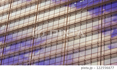 A facade of a modern skyscraper reflecting warm tones of sunset in its windows, interspersed with parallel metallic gridlines. A blend of urban architecture and the natural light soft hues 122556877