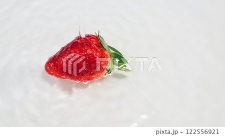 A vibrant red strawberry with a green leafy top is captured mid-splash in liquid, set against a smooth white background for a clean, fresh look. 122556921