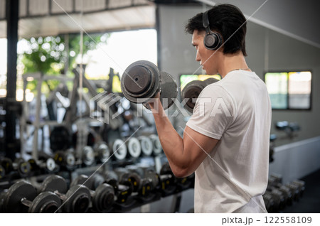 A man is enjoying the music through his headphones while working out with dumbbells in the gym. A man is enjoying the music through his headphones while working out with dumbbells in the gym. 122558109