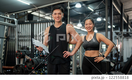 Two professional, confident Asian fitness instructors are standing in the gym. Two professional, confident Asian fitness instructors are standing in the gym. 122558818