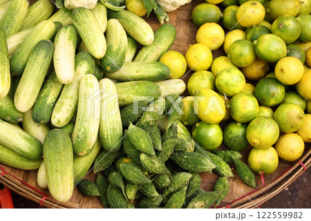 Different ripe vegetable in a wicker basket. Fresh cucumber, bitter gourd, lime for sale on street market, Southeast Asia. Fresh vegetables in a traditional morning market, Myanmar Different ripe vegetable in a wicker basket. Fresh cucumber, bitter gourd, lime for sale on street market, Southeast Asia. Fresh vegetables in a traditional morning market, Myanmar 122559982