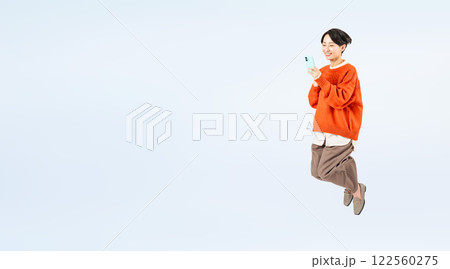 スマホを見ながらジャンプするおしゃれなミドル女性の全身写真 スマホを見ながらジャンプするおしゃれなミドル女性の全身写真 122560275