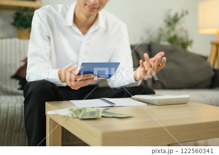 Smiling adult man sitting in a cozy living room checking his bankbook and calculating expenses 122560341