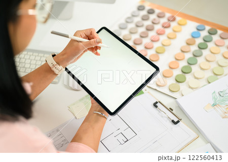 Designer working on digital tablet at desk surrounded by color samples, blueprints and design sketches Designer working on digital tablet at desk surrounded by color samples, blueprints and design sketches 122560413