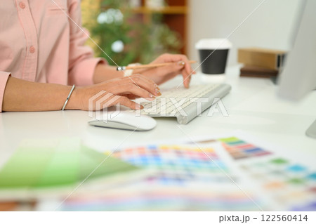 Close up of a designer hands typing on keyboard, surrounded by color swatches and design materials Close up of a designer hands typing on keyboard, surrounded by color swatches and design materials 122560414