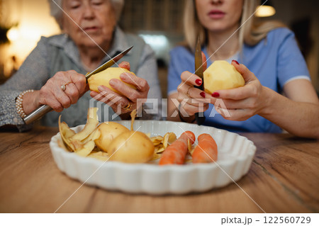 Portrait of elderly companion assistant and senior woman peeling potatoes. Home health care services. 122560729