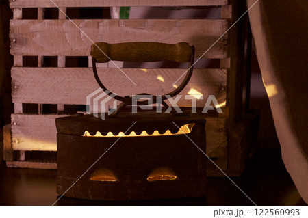 Old iron, heated by hot coals. In the twilight you can see the light of burning coals. Standing next to a wooden box. 122560993