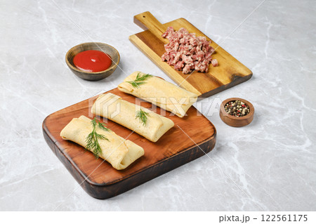 Three rolled crepes filled with seasoned ground meat are arranged on a wooden board 122561175