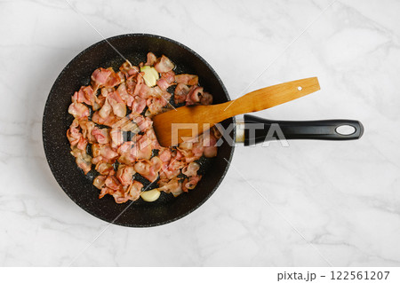 Cooking crispy bacon in a frying pan with a wooden spatula on a marble countertop Cooking crispy bacon in a frying pan with a wooden spatula on a marble countertop 122561207