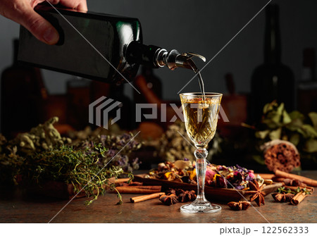 Yellow herbal liquor or mixture is poured from a vintage bottle into a glass. 122562333