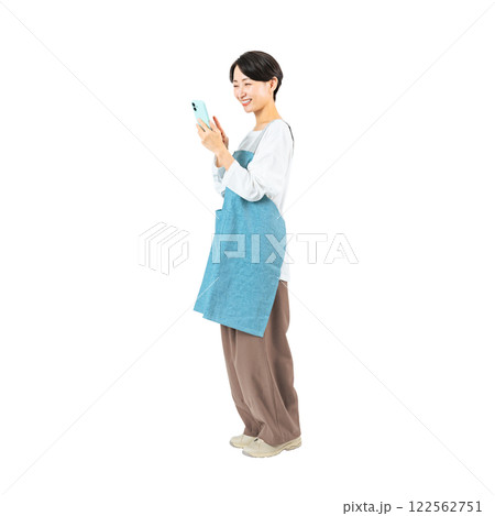 笑顔でスマホを使うエプロンをつけたミドル女性　手作業で精密に切り抜いた背景透過全身写真PNG 122562751