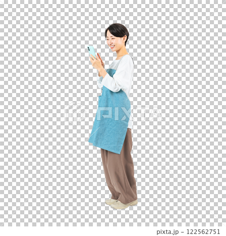 笑顔でスマホを使うエプロンをつけたミドル女性　手作業で精密に切り抜いた背景透過全身写真PNG 122562751