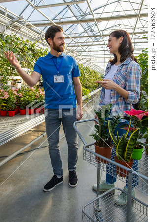 Salesman at retail store offering potted plants and flowers to woman customer 122563603