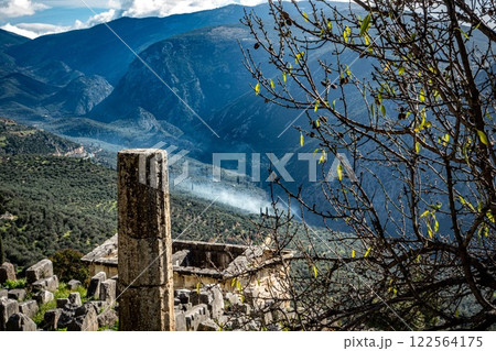Ancient Delphi. Delfos column on slope with smoke and valley. Greece Ancient Delphi. Delfos column on slope with smoke and valley. Greece 122564175