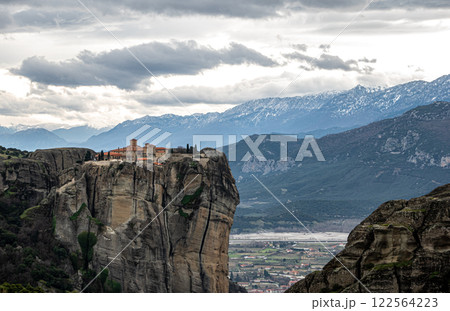 A cliff with a monastery on top, surrounded by majestic mountains in Meteora 122564223