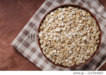 Raw Rolled Oats in Clay Bowl on Checkered Linen Napkin, Top View, Copy Space 122564887