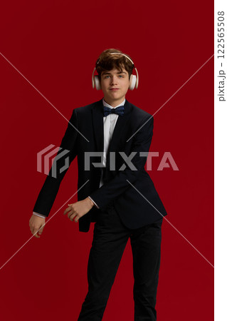 Portrait of positive young man, student in formal wear and bow tie, listening to music in headphones and dancing with joy and fun Portrait of positive young man, student in formal wear and bow tie, listening to music in headphones and dancing with joy and fun 122565508