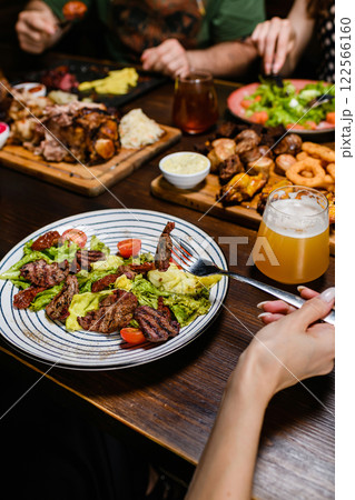 A person holds a fork with a bite, while beer and various dishes on a table. A person holds a fork with a bite, while beer and various dishes on a table. 122566160