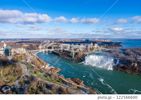 Niagara Falls City, Ontario, Canada - December 19 2021 : Overlooking the Niagara River Rainbow Bridge and American Falls in a sunny day. 122566600