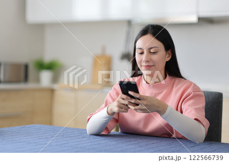 Satisfied asian woman using smart phone in a kitchen Satisfied asian woman using smart phone in a kitchen 122566739