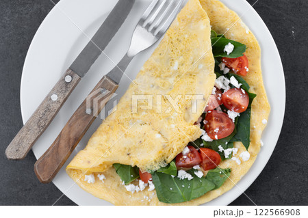 Stuffed omelette with tomatoes and spinach on black slate background 122566908