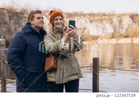 Young couple in love taking a photo. Millennial guy and girl enjoying autumn day out laughing at camera together. Selfie of a young couple in the mountains by the river. Lifestyle and tourism concept. 122567539