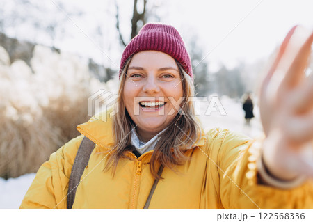 Smiling woman in winter clothing taking photo on park background. Selfie time. Holidays, rest, blogging banner. Charming female wearing stylish outfit have fine 122568336