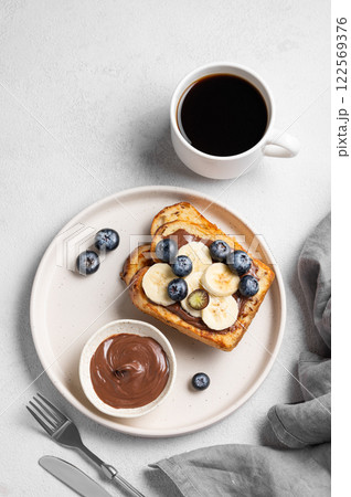 Toasted bread with chocolate cream, blueberries and banana on a plate on a light background 122569376