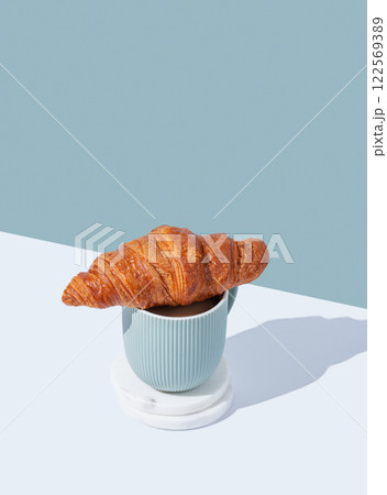 Fresh croissant on a cup of cappuccino or latte coffee on white and blue  background with shadow. 122569389