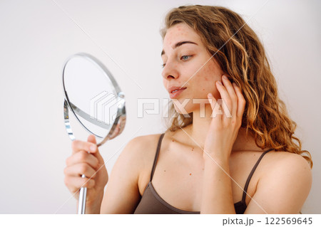 Beautiful woman with problematic skin looks in her small mirror. Cosmetology. Skin care concept. Beautiful woman with problematic skin looks in her small mirror. Cosmetology. Skin care concept. 122569645