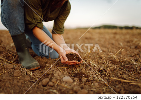 A young woman farmer holds black soil in hand on an agricultural field. Fertility concept, scaling. 122570254