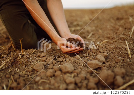 A young woman farmer holds black soil in hand on an agricultural field. Fertility concept, scaling. 122570255