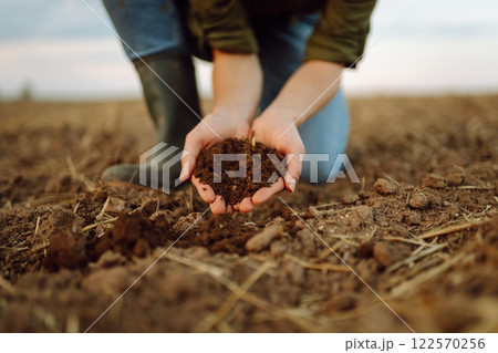 A young woman farmer holds black soil in hand on an agricultural field. Fertility concept, scaling. 122570256