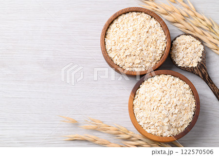 Oat flakes in wooden bowl and spoon on white background with copy space Oat flakes in wooden bowl and spoon on white background with copy space 122570506