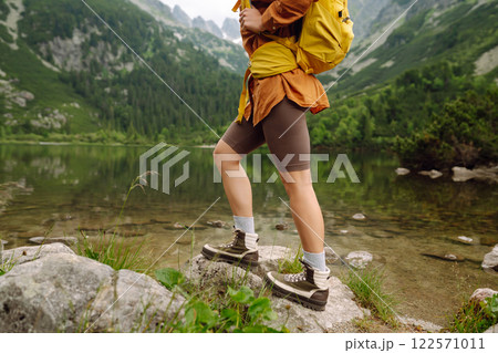 Travel Slovakia, Europe. Tourist with a yellow backpack stands against the backdrop of alpine lake. Travel Slovakia, Europe. Tourist with a yellow backpack stands against the backdrop of alpine lake. 122571011