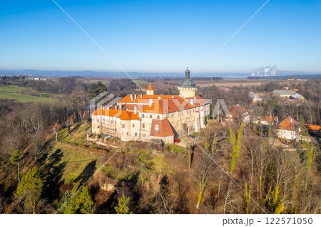 Grabstejn Castle stands majestically under a clear blue sky, surrounded by lush trees and beautiful landscapes. Sunlight highlights its historical architecture and vibrant rooftops. 122571050