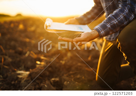 Farm owner checks quality of soil with his hands with tablet and checks fertility before sowing. 122571203