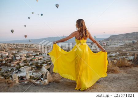 Woman stands on mountain with flying air balloons on background. Tourist Turkish region Cappadocia. Woman stands on mountain with flying air balloons on background. Tourist Turkish region Cappadocia. 122571821