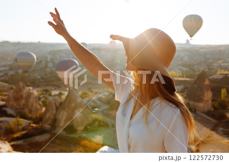 Woman stands on mountain with flying air balloons on background. Tourist Turkish region Cappadocia. Woman stands on mountain with flying air balloons on background. Tourist Turkish region Cappadocia. 122572730